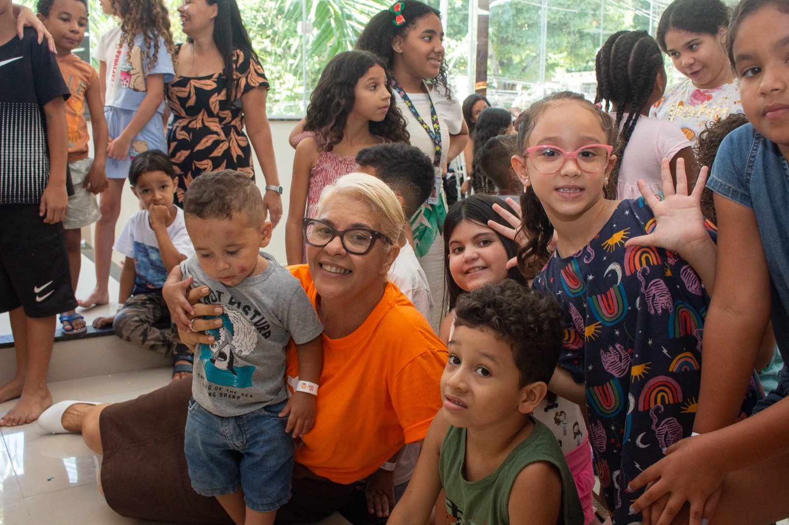 Voluntária sorrindo cercada de crianças acenando e felizes na festa do Amor e Vida