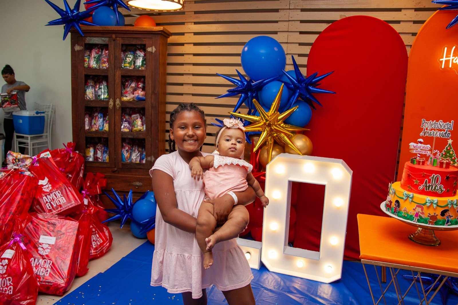 Menina segurando bebê ao lado das sacolas de presente